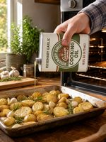 Pouring Rosemary Garlic tallow oil over a roasting tray of potatoes and garlic